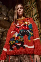 Sweater tejido a mano con lana color ladrillo, cuello redondo, puños y ruedo acanalados con rayas blancas. Presenta bordados con figuras de personas y animales.