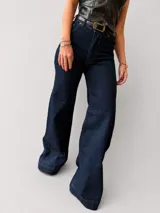 Jean de corte wide leg y tiro alto, confeccionado en denim azul oscuro. Presenta un diseño de pierna amplia y recta con costuras reforzadas en el ruedo.