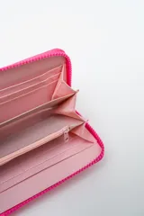 Billetera rectangular con cierre, color celeste pálido, con parche frontal negro que lleva las letras "CNJ" en relieve. Incluye un llavero de muñequera con cordón trenzado en rosa fuerte y verde lima.