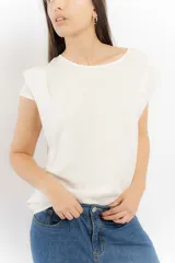 Remera sin mangas de corte holgado, con hombreras marcadas que crean un efecto de manga corta estructurada. Presenta un diseño minimalista con frunces laterales en la cintura y cuello redondo.