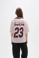 Remera tipo chomba de manga corta con cuello camisero, confeccionada en tejido con estampado de tablero ondulado en tonos rosado y blanco, con franja horizontal y detalles gráficos en color bordó.