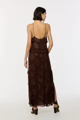 Vestido largo marrón de viscosa con estampado paisley formado por apliques termoadhesivos dorados. Presenta escote en V con tirantes finos, volantes en cascada y una abertura lateral profunda en la falda.