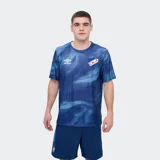 Remera deportiva Umbro modelo Press, de color rojo con un estampado abstracto en tonos más oscuros, cuello redondo y manga corta. Incluye el logo de la marca en el pecho y el escudo del Club Nacional de Football.
