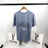 Remera celeste de algodón con estampa en la espalda con el texto "SAMPLE" y el logo de la marca DUXON.