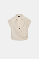 Camisa color crudo confeccionada con lino, de corte holgado, cuello solapa y escote en V. Tiene manga sisa y detalle de pliegue en el delantero. Cierre frontal con botón.