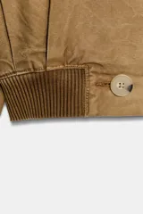 Trench corto de cuello solapa y manga larga, con diseño cruzado y cierre frontal con botones. Presenta bajo acabado en elástico y trabillas en los hombros.