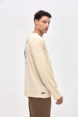 Remera de manga larga color beige, confeccionada en algodón lavado con textura suave. Presenta cuello redondo con detalle de costura en V, corte clásico y estampado pequeño en el pecho con la palabra Uniform.