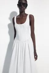 Vestido midi de corte corsetero color blanco, con escote redondo, tirantes finos y detalle de lazo en el delantero. Falda con frunces y cierre en la espalda con cremallera oculta.