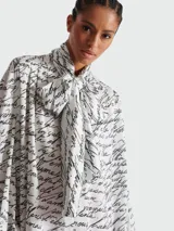 Camisa blanca con estampado de texto en negro, lazo en el cuello y mangas largas abullonadas.