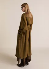 Trench coat de corte oversize y diseño largo en color verde oliva. Presenta cierre de doble botonadura, cuello con solapas de muesca, trabillas en hombros y mangas, y cinturón desmontable a tono. Incluye forro interior y abertura posterior en el bajo.