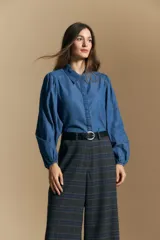 Camisa de denim azul con cuello camisero, cierre frontal de botones y mangas largas abullonadas con hombros fruncidos.