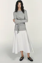 Vestido midi de cuello redondo y manga larga, con la parte superior gris y la falda blanca. La parte superior presenta un detalle de tejido superpuesto ajustable con lazada en la cintura. La falda es de tipo gabardina.