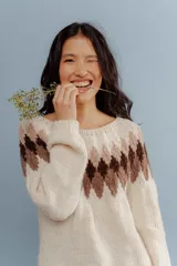 Buzo de lana merino color crudo, con diseño de rombos geométricos en tonos marrones y beige en la parte superior y las mangas, cuello redondo y manga larga.