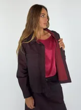 Chaqueta tipo camisa de denim color borgoña, con cuello clásico, manga larga, cierre frontal con botones y bolsillo de parche en el pecho.