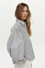 Camisa de algodón con rayas verticales grises y blancas, cuello camisero, mangas largas abullonadas y cierre frontal con botones.