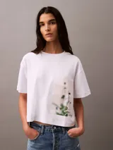 Remera blanca de algodón con corte cropped y mangas cortas. Presenta un estampado fotográfico floral de Calvin Klein en el lateral.