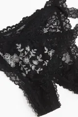 Pack de dos bombachas tipo thong de encaje negro. Una presenta un bordado floral en blanco en la parte delantera, mientras que la otra es completamente de encaje negro. Ambas son de tiro bajo con laterales finos y tienen refuerzo interior.