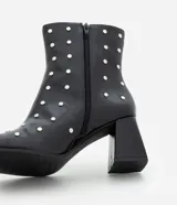 Bota de caña corta confeccionada en poliuretano color negro, con punta cuadrada, taco bloque y aplicación de studs metálicos en toda la superficie. Cuenta con cierre lateral.