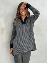 Sweater de punto con rayas verticales en gris y negro, cuello en V con solapa negra, mangas largas con puños negros y corte asimétrico.