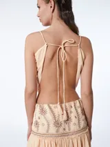 Conjunto de top corto y falda larga color durazno, con bordados florales en tonos marrones. El top tiene escote en pico y tirantes finos. La falda es de corte amplio y tiene volantes en el ruedo.