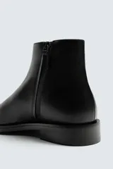 Bota de piel negra con diseño minimalista, cierre de cremallera lateral, horma cuadrada y suela a tono con ligero tacón.