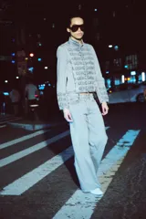 Chaqueta de denim con efecto lavado, corte entallado y cuello redondo. Presenta un diseño de estilo militar con cierre frontal de cremallera metálica y aplicaciones decorativas de botones y costuras en el delantero y los puños.