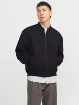 Campera bomber negra Jack & Jones de tejido plano liviano, con cuello baseball, cierre frontal de cremallera, bolsillos delanteros y puños de canalé. Confeccionada en poliéster y poliéster reciclado.