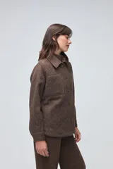 Camisa de lana fina sin teñir, color marrón, con diseño capitoneado y pespuntes decorativos. Presenta cuello clásico, cierre frontal con botones metálicos y dos bolsillos frontales tipo parche.