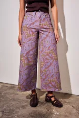 Pantalón jean de tiro alto y corte wide leg, con estampado de hojas grandes en tonos morados y fondo con patrón a cuadros.