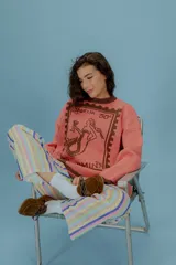 Buzo oversized color rosa salmón con cuello redondo y puños marrones. Presenta un estampado tejido en color marrón que simula un sello postal con una sirena.