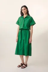 Vestido camisero midi verde esmeralda con cuello camisero, mangas cortas con puños, cierre frontal con botones y cinturón de lazo a juego.