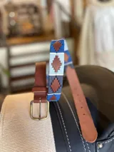 Cinturón de cuero marrón con hebilla metálica rectangular y detalle de bordado artesanal en tonos azules y celestes con diseño geométrico.
