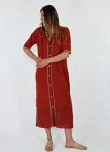 Vestido midi de punto color ladrillo, con cuello camisero, manga corta, botonadura frontal completa y detalles de costuras decorativas contrastantes en beige. Presenta un diseño calado en el dobladillo inferior.