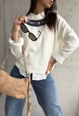 Sweater de punto color natural con cuello redondo y detalle de guarda tejida en la parte superior del pecho. Presenta mangas largas con puños acanalados y un diseño de corte recto.
