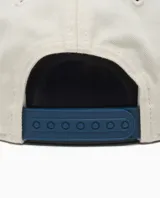 Gorra de béisbol de cinco paneles, color crema con visera azul marino. Presenta bordado en el frente con el texto "Carhartt WIP in the hearts of many since 1989" en hilo azul.