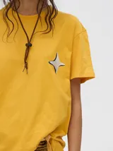 Remera amarilla de ajuste holgado y corte cuadrado, con cuello redondo, mangas cortas y estampa de estrella de cuatro puntas en el pecho.