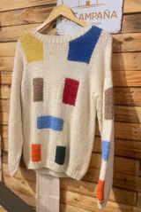 Buzo tejido a mano de lana 100% merino, color off-white con diseño de formas geométricas abstractas y coloridas de estilo artesanal, con cuello redondo y mangas largas.