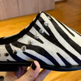 Suecos chatos de cuero con estampado animal print de cebra, punta cuadrada y detalles de tachas metálicas en los laterales.