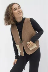 Chaleco reversible confeccionado en cuero genuino. Presenta un lado de piel de oveja gris con bolsillos de cuero negro y un lado de cuero liso gris. Diseño sin mangas con cierre frontal.