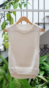 Chaleco tejido de punto en lana merino, color crudo, con cuello redondo y diseño sin mangas. Presenta un corte recto con terminaciones acanaladas en el cuello, sisas y ruedo.
