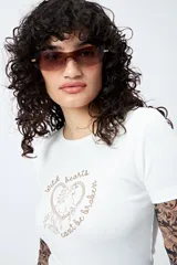 Remera blanca de corte ajustado con cuello redondo y mangas cortas. Presenta una estampa frontal en color marrón con el texto 'Wild hearts can't be broken' y un diseño de caballo dentro de un corazón.