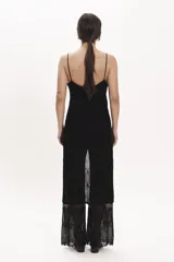 Pantalón de tejido de punto negro, corte ancho y tiro alto, con detalle de encaje calado en la parte inferior. Se lleva debajo de un vestido largo de encaje negro con tirantes finos y botones frontales.