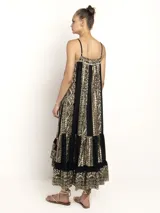 Vestido negro de breteles finos con escote en V y silueta amplia. Presenta un estampado geométrico en dorado que recorre paneles verticales y un ruedo con volado.