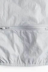 Campera deportiva liviana color gris, resistente al agua, con cuello elevado y cierre frontal. Cuenta con tecnología DryMove para absorber el sudor, mangas largas con puños elásticos y diseño plegable.