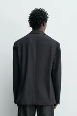 Blazer relaxed fit de estructura color gris, confeccionado en tejido con algodón, cuello con solapas de muesca, manga larga con botones en los puños y bolsillos de plastrón en la cadera.