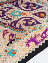 Bandana cuadrada de satén con estampado de arabescos en tonos violeta, naranja, celeste y blanco, con borde negro.