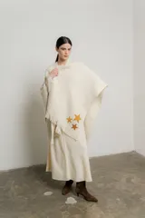 Ruana de tejido de punto color crudo, con flecos en el ruedo y apliques de estrellas bordadas a mano en tonos dorados y ocres.