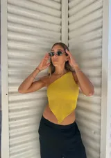 Top tejido de punto color amarillo, con diseño asimétrico de un solo hombro y terminación en punta en el ruedo inferior.