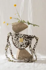Bandolera con silueta de media luna y estructura rígida, confeccionada en cuero con estampado animal print tipo vaca. Presenta herrajes metálicos en tono bronce, cierre superior y correa regulable que permite su uso al hombro o cruzada. Incluye una placa metálica decorativa con iniciales en el frente.