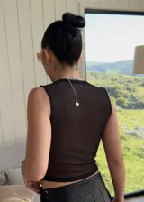 Top sin mangas de tul negro, con diseño reversible que permite variar la transparencia entre el frente y la espalda. Presenta un corte ajustado al cuerpo y cuello redondo.